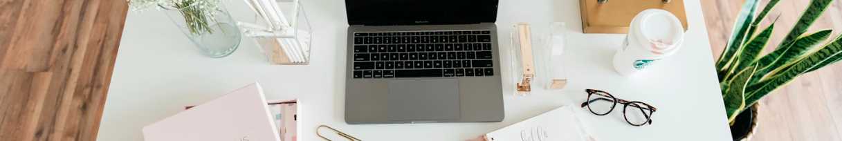 An organized desk with a notebook, planner, computer, and plants